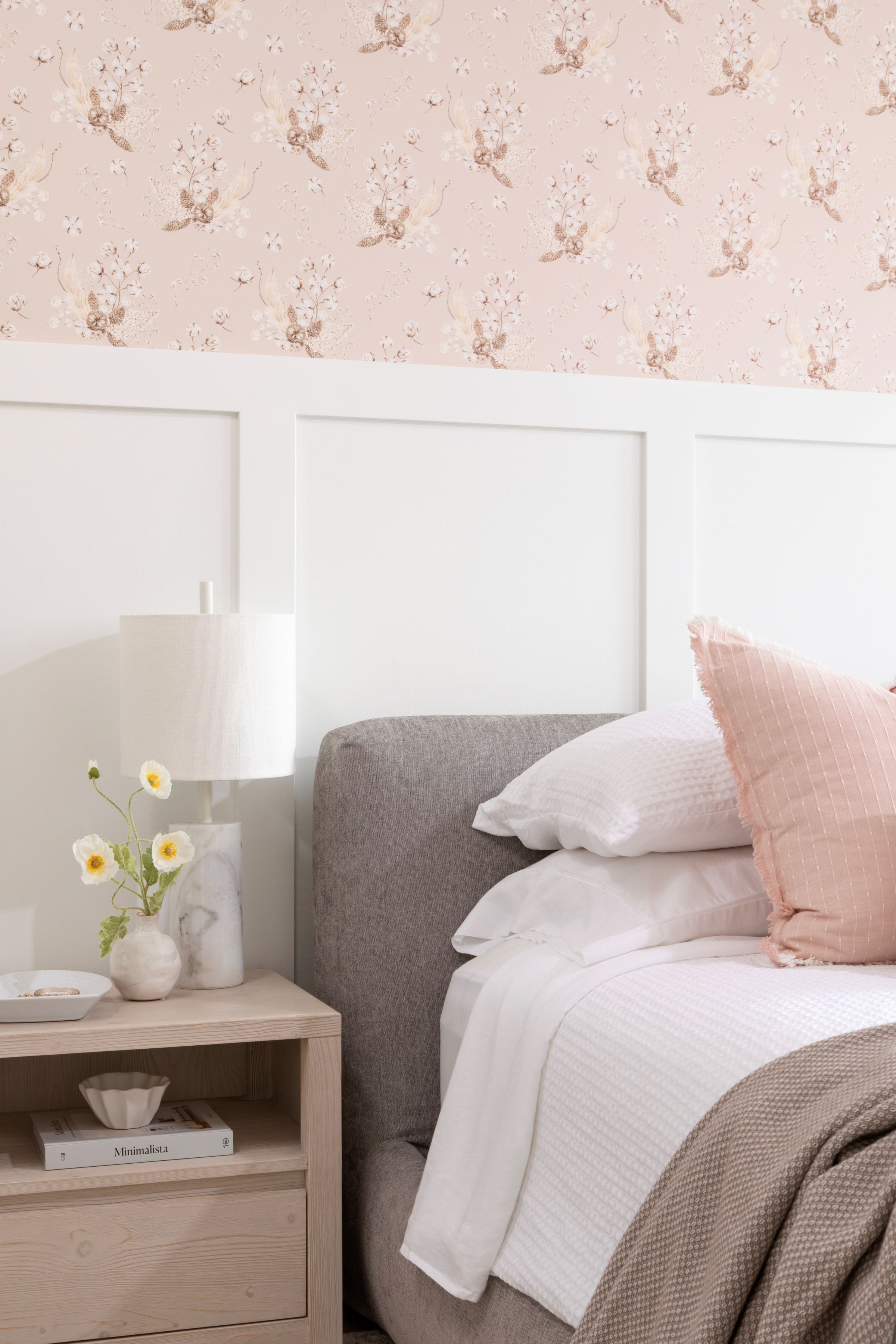 A cozy bedroom corner with 'Boho Bouquet II Wallpaper' above the wainscoting, creating a warm, bohemian vibe. The wallpaper's blush and gold floral motifs harmonize with the room’s soft textiles and wooden bedside table, crafting an inviting, stylish space.