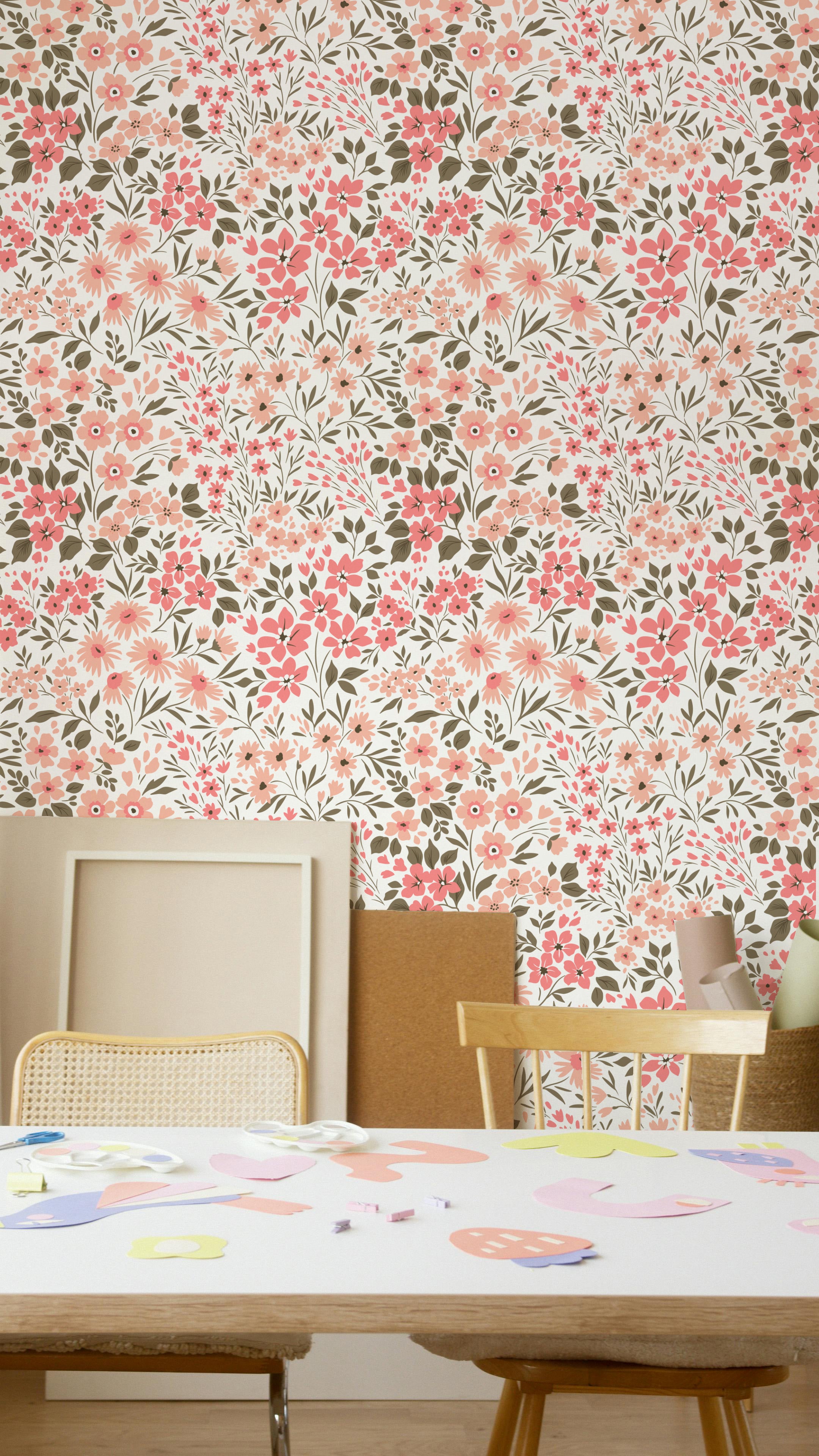 A creative space with a table covered in paper cutouts and crafts supplies, surrounded by chairs. The background wall is adorned with the Floral Frenzy Wallpaper, which has a lively pattern of pink, peach, and beige flowers amidst green leaves.
