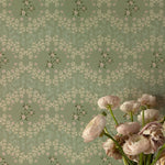Detail view of the Heritage Blooms Wallpaper, highlighting its intricate floral design in soft green, embellished with small white and pink flowers. A bouquet of pale pink flowers in the foreground adds a touch of natural beauty, complementing the wallpaper's vintage charm.