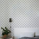 Modern bedroom interior featuring walls covered with Tiny Hydrangea wallpaper. A minimalist white bedside table holds a small plant, under a stylish black wall-mounted lamp, next to a neatly made bed with gray bedding.