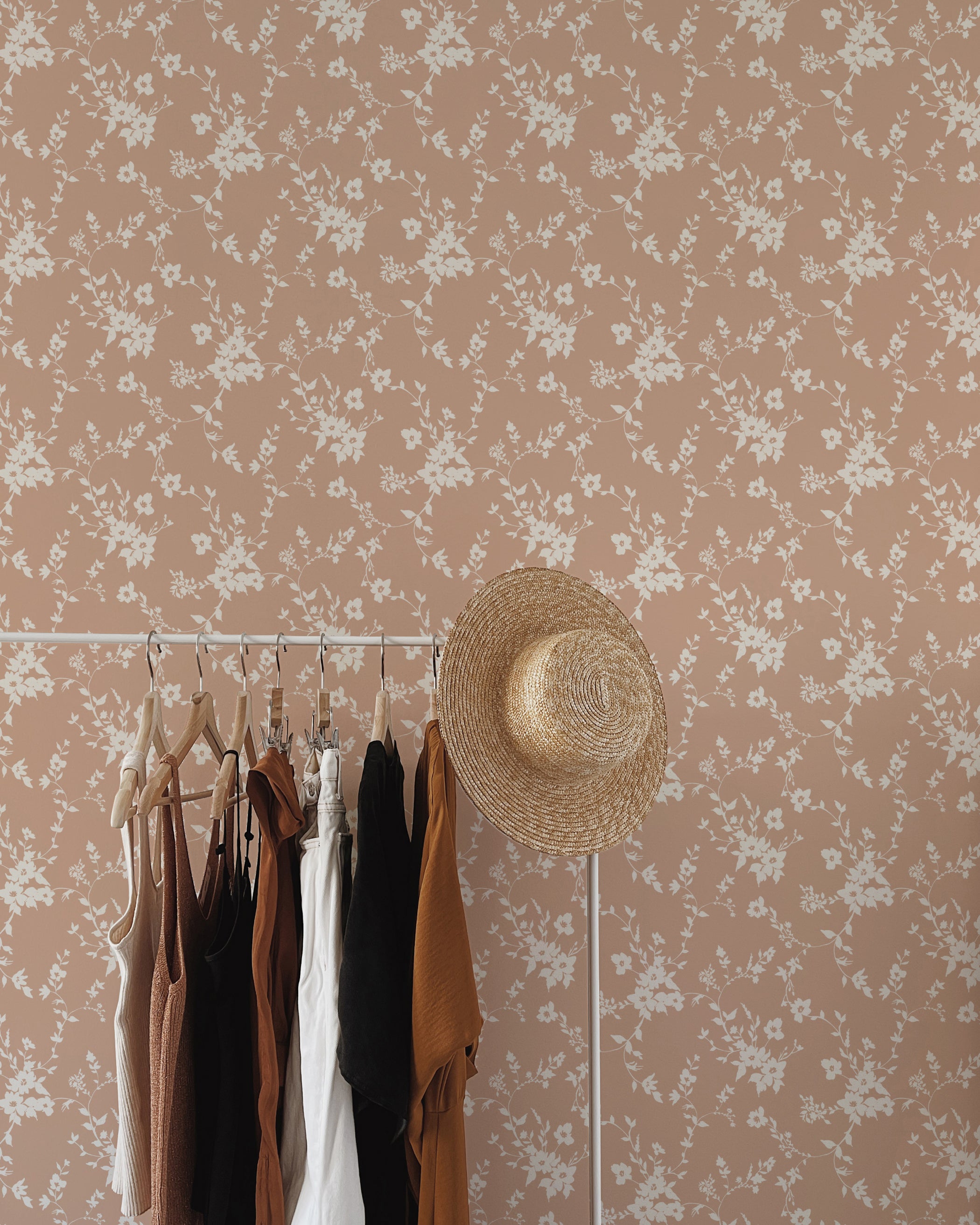 A stylish dressing area with a rack of fashionable clothes in natural tones, a straw hat, and a wall adorned with delicate pink floral wallpaper, creating an elegant and feminine ambiance.