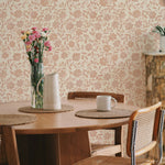 Dining area with Whimsy Blooms Wallpaper, showcasing a delightful floral pattern in soft pink hues, complementing the wooden furniture and creating a warm, inviting ambiance.