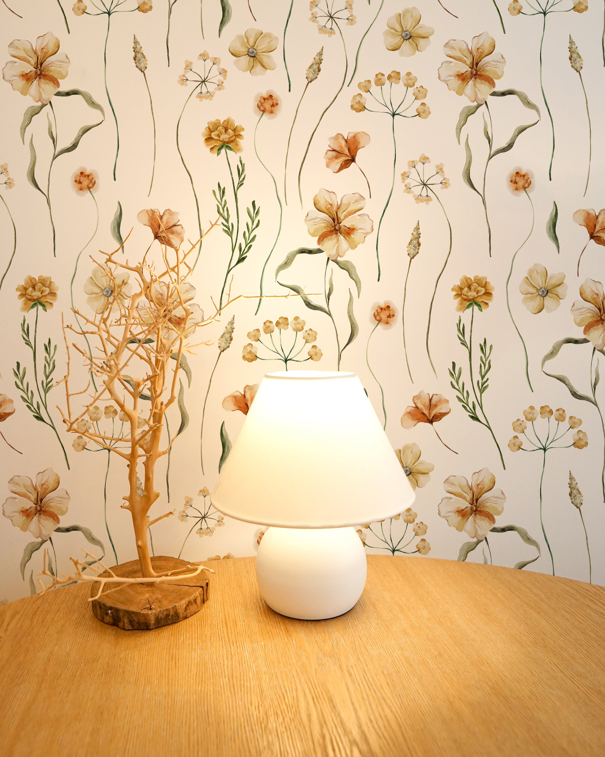 A serene bedside setup with the Warm Glow Floral Wallpaper providing a tranquil background. A simple white lamp on a wooden nightstand complements the wallpaper’s floral motifs, creating a peaceful and relaxing bedroom ambiance