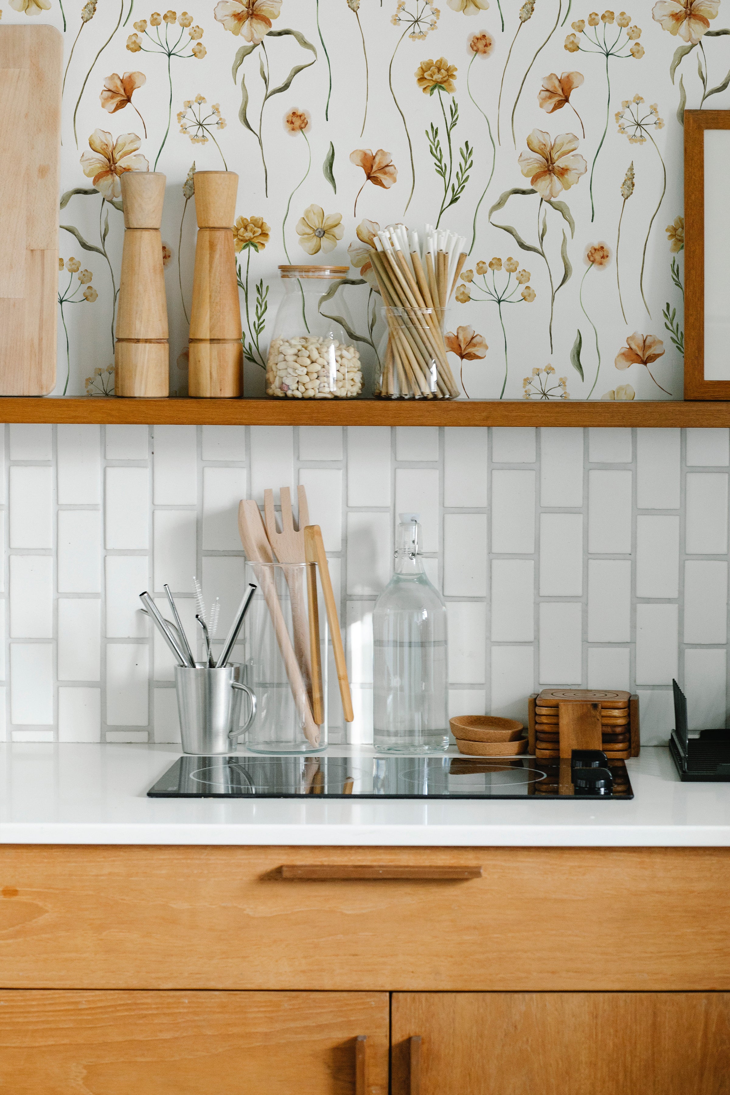A modern kitchen enhanced by Warm Glow Floral Wallpaper, featuring a subtle and elegant floral pattern. Wooden kitchen accessories and white tiles complement the wallpaper's soft, natural color palette, creating a harmonious and inviting cooking space.