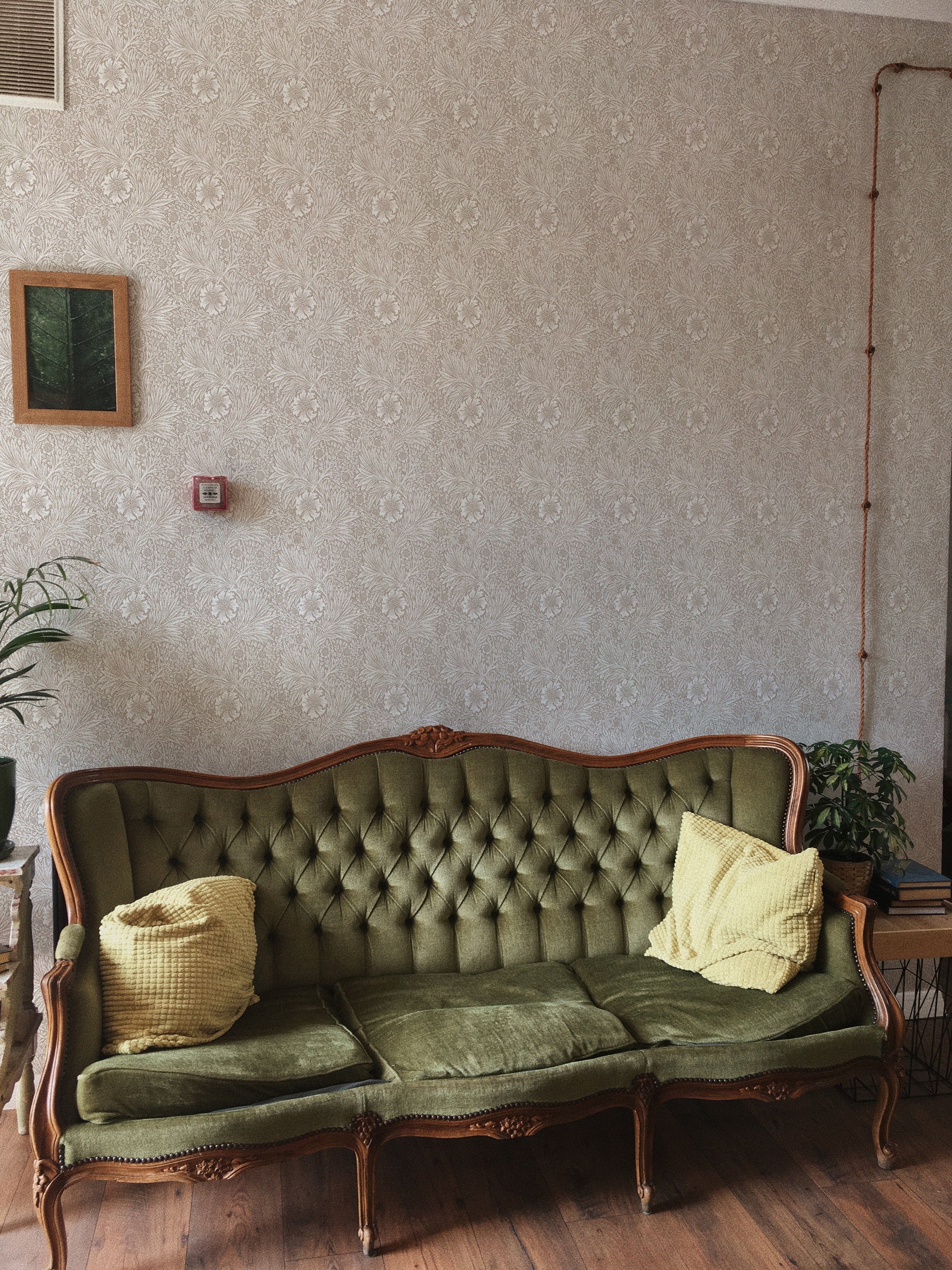 Classic living room corner decorated with Timeless Floral Wallpaper, showcasing soft beige floral designs behind a vintage tufted green velvet sofa.