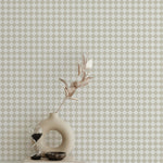 A stylish decor arrangement with a beige sculptural vase holding a dried leaf stem, an hourglass, and a small bowl placed on a white surface. The wall behind features beige and white checkered wallpaper, enhancing the space with its classic and refined pattern