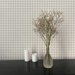 A minimalist setting featuring a black surface with two white candles and a clear vase holding delicate dried flowers. The background showcases beige and white checkered wallpaper, adding a subtle and elegant pattern to the scene.