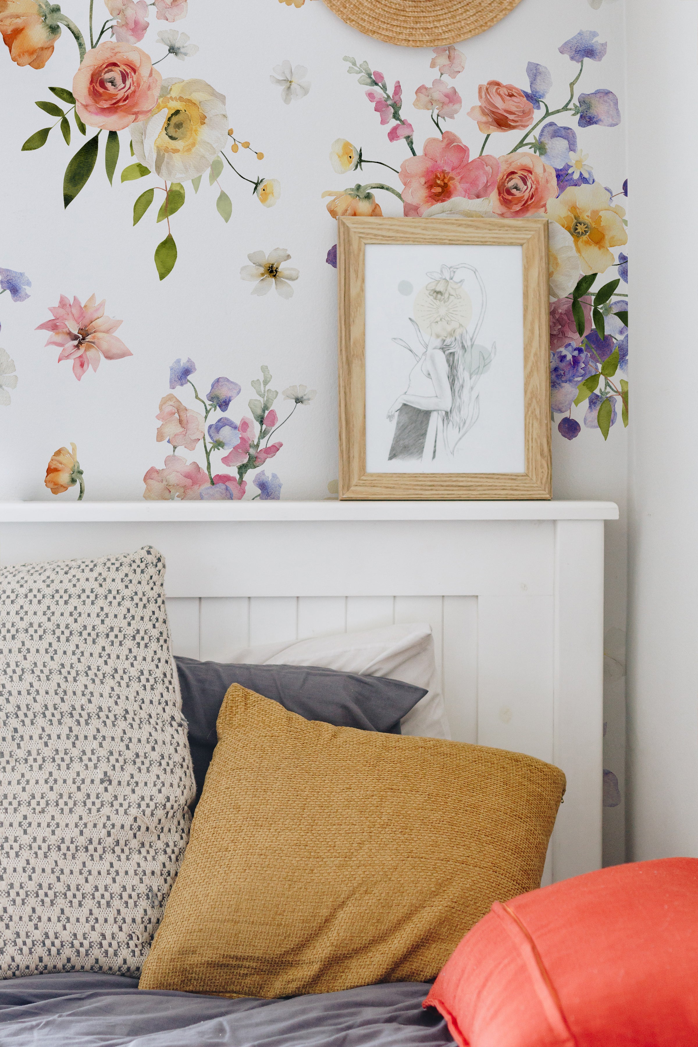A cozy corner of a bedroom showcasing the Bouquet Bliss Wallpaper. This intimate space is styled with a rustic wooden headboard and a mix of colorful pillows. The wallpaper's floral pattern adds a fresh and whimsical touch to the room, complementing the simple and warm bedding
