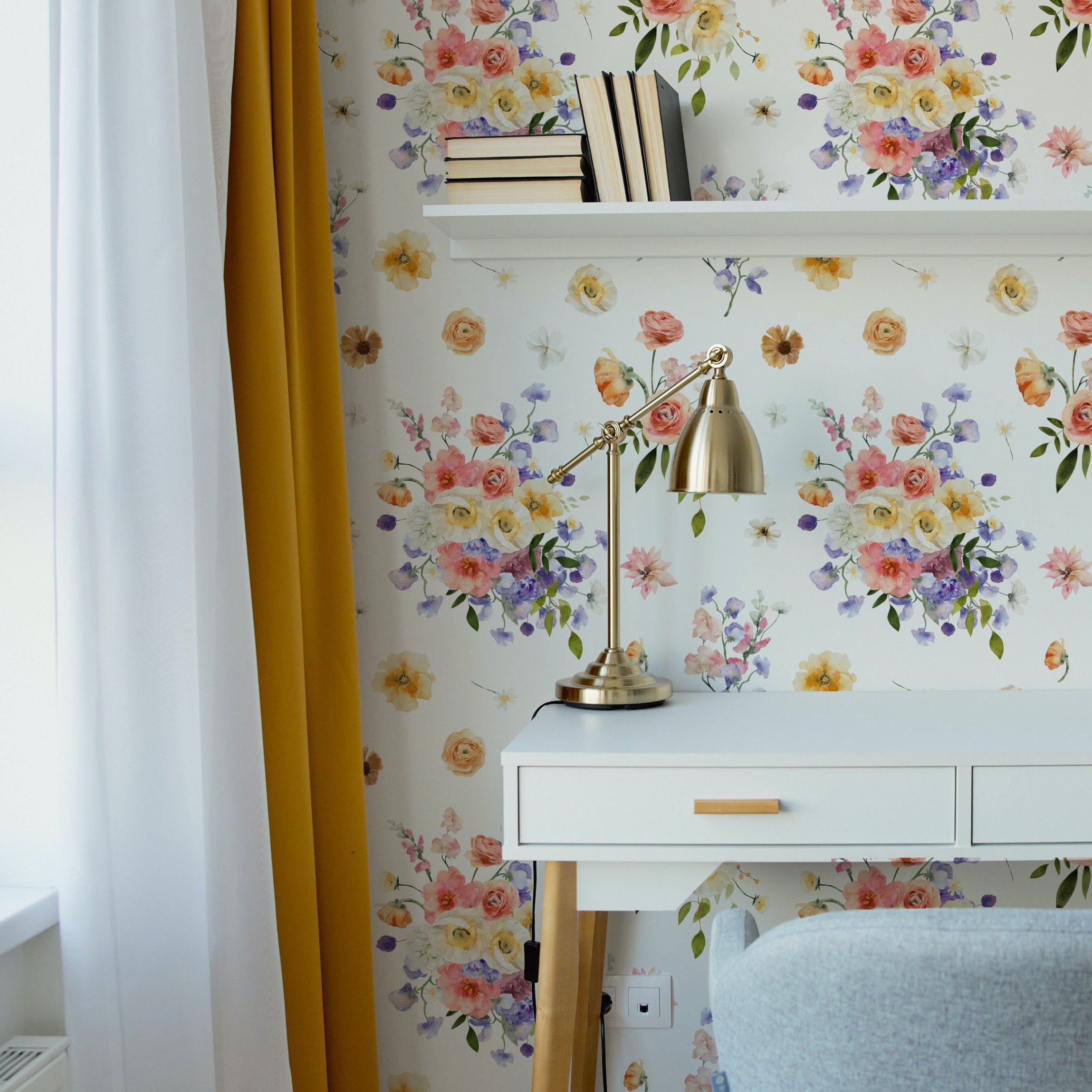 A bright and vibrant home office space adorned with Bouquet Bliss Wallpaper, featuring a lively floral design with large clusters of colorful flowers. The workspace includes a white desk with a gold lamp and is accented by a yellow curtain, enhancing the cheerful and inviting atmosphere.