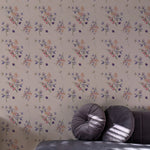 Violet Bloom Wallpaper with a pattern of delicate, pastel-colored flowers on a nude background, adorning a wall behind a plush grey sofa with round cushions.