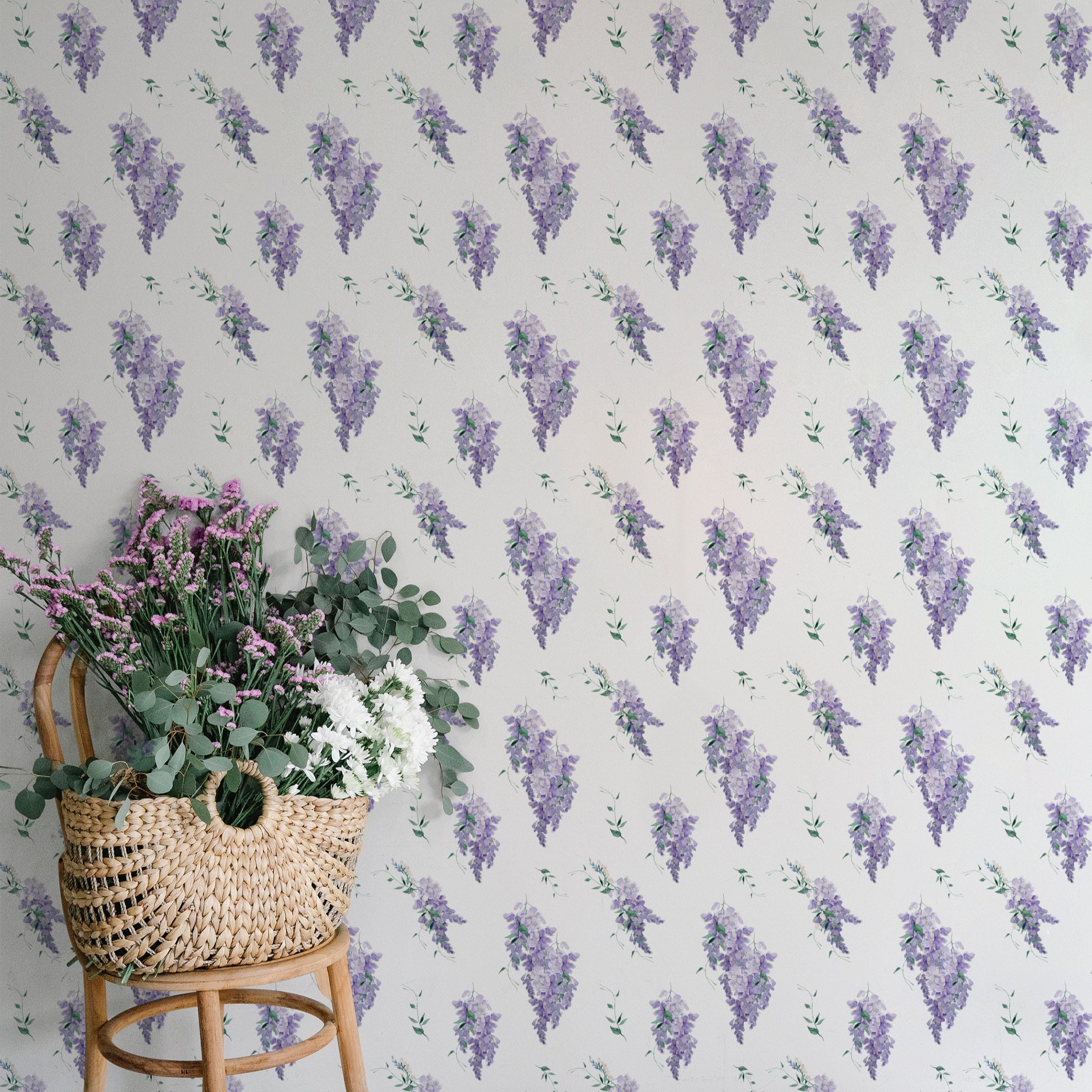 A charming interior setting with the Wisteria Garden Wallpaper as the backdrop. A rustic woven basket filled with a variety of fresh greenery and flowers sits on a wooden chair, highlighting the natural theme.