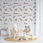 A playful children's room featuring 'Floral Bunnies Wallpaper' with whimsical illustrations of rabbits in various poses, decorated with pastel-colored floral patterns. The room includes a small wooden table and chairs set, a toy chest, and a soft, round rug, creating a charming and inviting play area