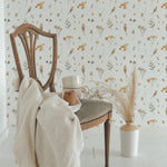 An elegant vintage chair draped with a cozy cream knit blanket sits in front of a wall covered in Buttercup Fields Wallpaper, showcasing a whimsical pattern of yellow buttercup flowers and soft gray foliage on a white background.
