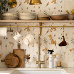 A charming kitchen corner with open shelving displaying ceramics and wooden utensils. The Buttercup Fields Wallpaper lines the wall behind a farmhouse sink, providing a cheerful and rustic backdrop with its yellow and gray botanical print.