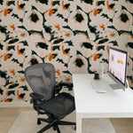 An office space decorated with Abstract Fields Wallpaper, which exhibits a lively abstract pattern with splashes of black and orange on a beige backdrop. The office setup includes a modern desk with a computer, a comfortable office chair, and a cozy white rug, creating a stimulating and creative workspace.