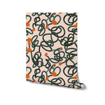 Rolled up view of Abstract Scribble Wallpaper showing off its chaotic yet charming pattern of dark green loops and orange blooms against a peach-colored background, ready to bring a lively and artistic vibe to any interior space.