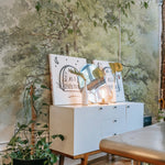 A creative workspace enhanced by the Boomstudie Vintage Wall Mural, showcasing a sprawling tree with lush foliage. The naturalistic detail of the mural adds depth and a sense of tranquility to the room, complementing the modern and minimalist furniture.