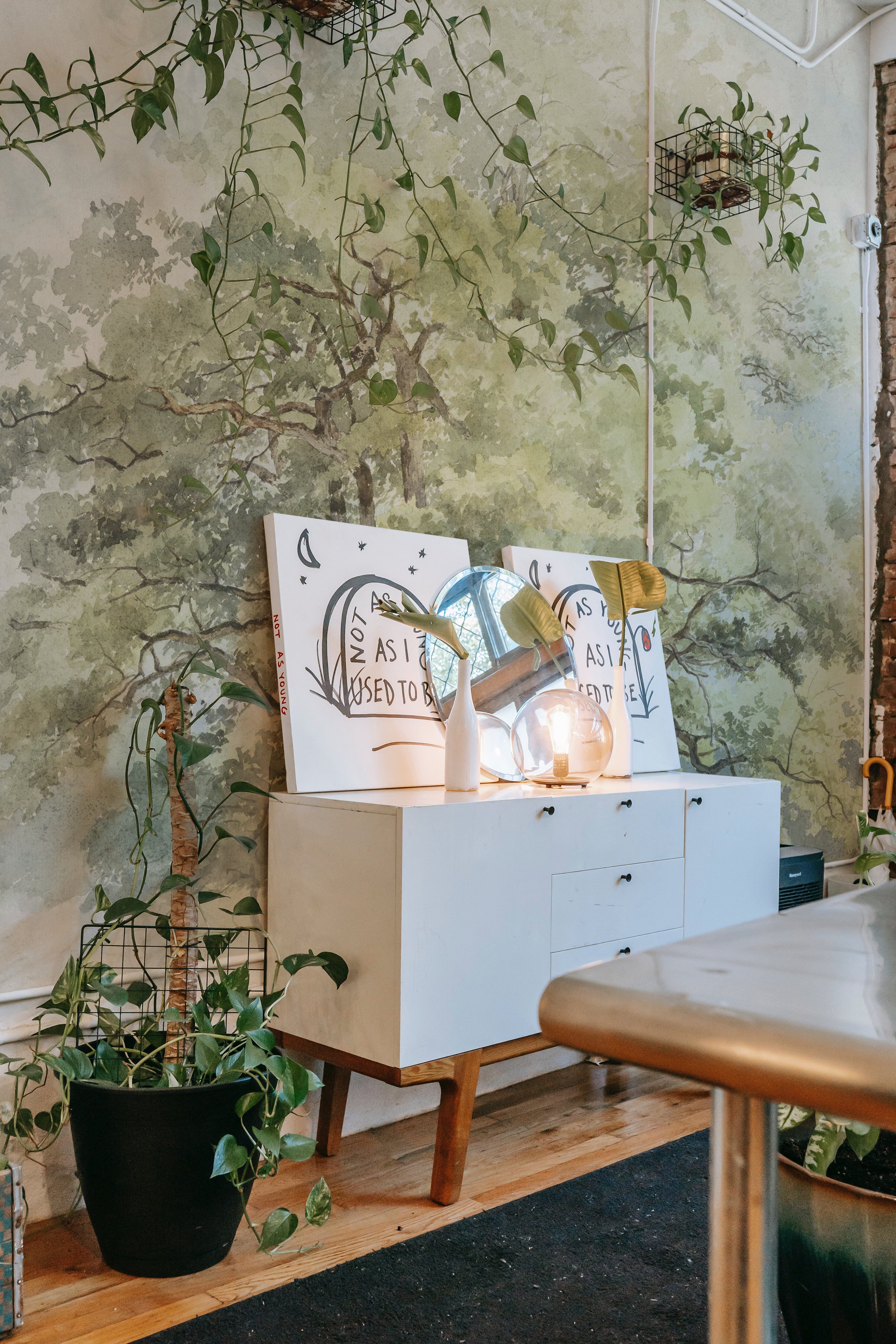 A creative workspace enhanced by the Boomstudie Vintage Wall Mural, showcasing a sprawling tree with lush foliage. The naturalistic detail of the mural adds depth and a sense of tranquility to the room, complementing the modern and minimalist furniture.