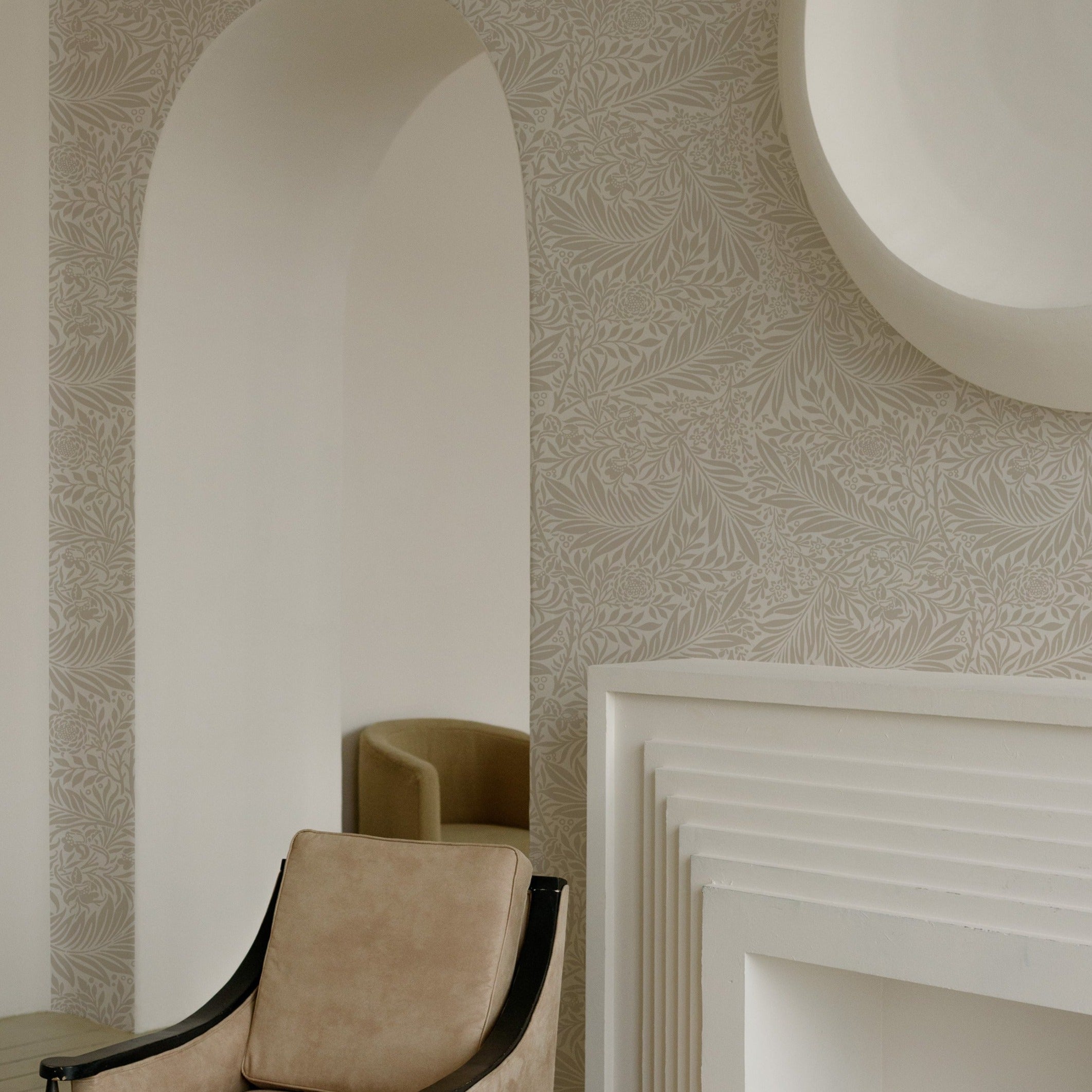 A cozy nook featuring the 'William Bough Wallpaper' with a detailed botanical design behind an archway, complemented by a modern armchair and an elegant white fireplace