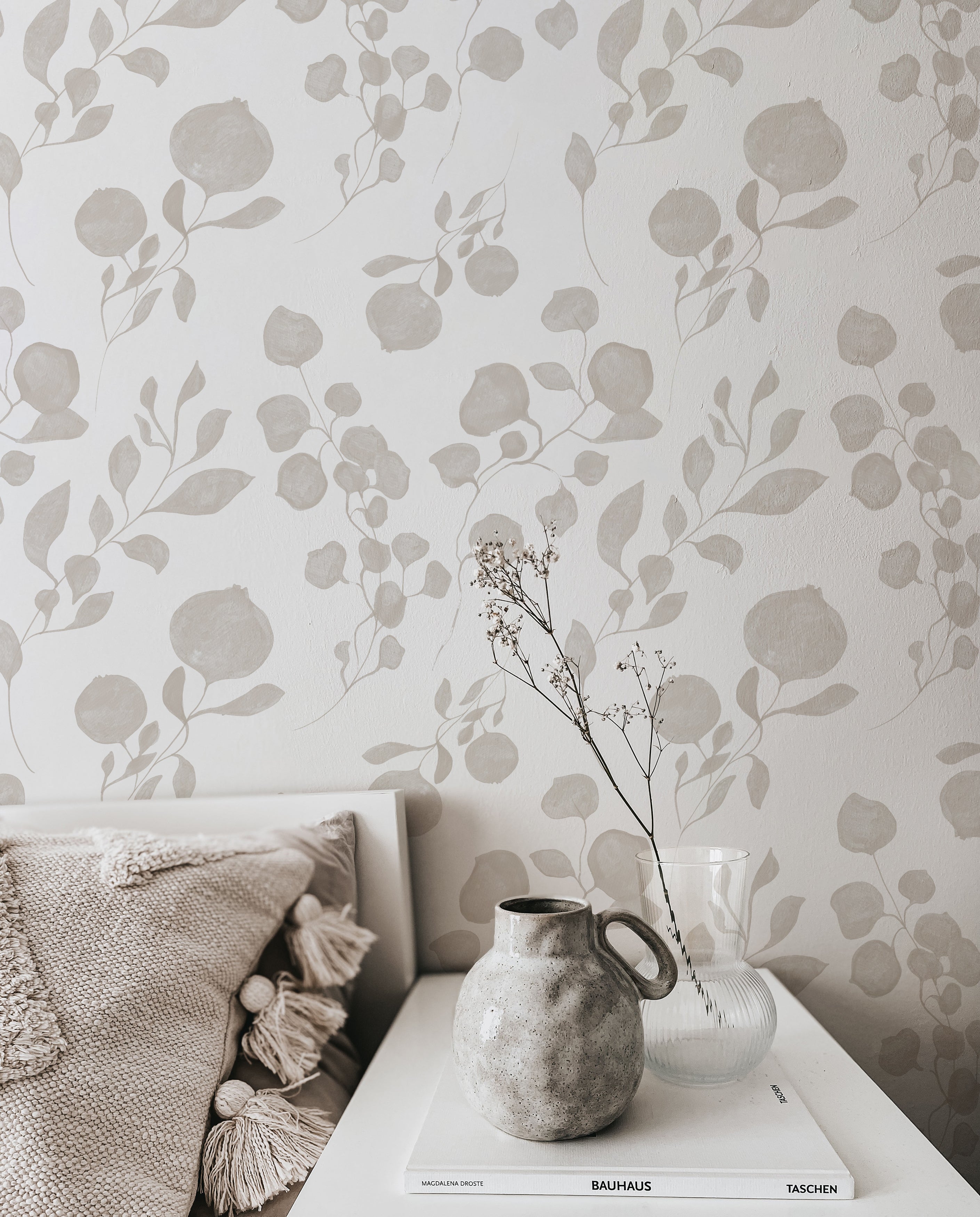 A cozy corner of a room showing the "Atelier Botanique Wallpaper" as a wall accent. A plush pillow and a rustic vase with dried flowers sit atop a side table, highlighting the wallpaper's ability to complement a peaceful and refined interior décor.
