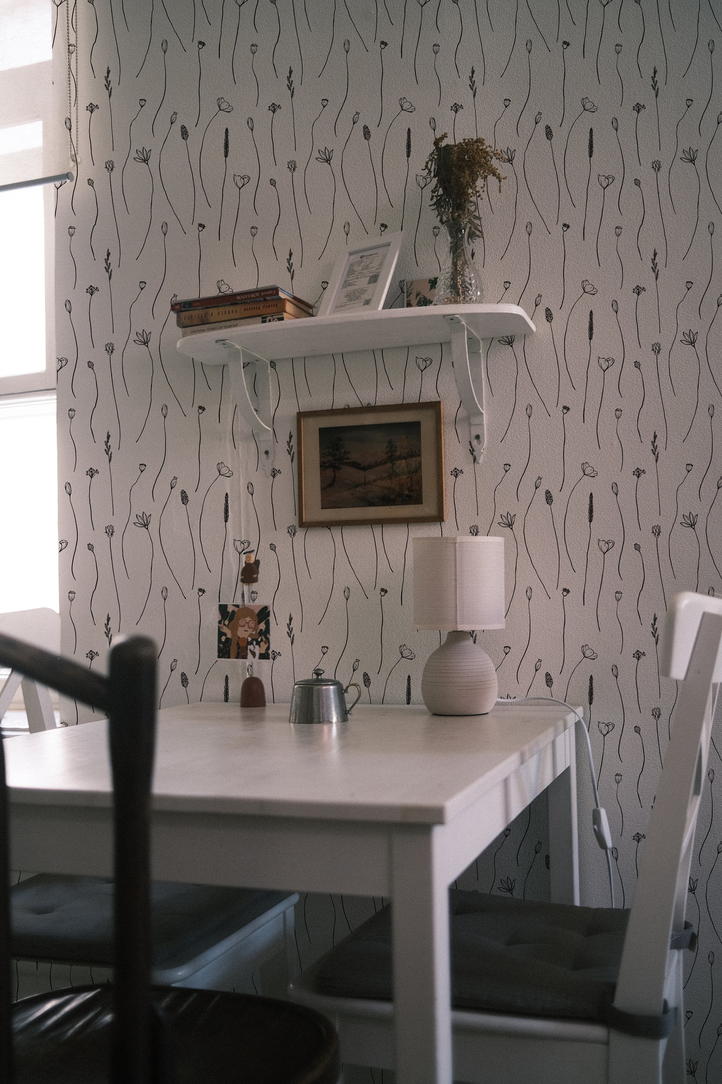 A cozy dining area enhanced with the 'Wildflower Sketch Wallpaper' featuring a simple black and white line art of wildflowers. The elegant, minimalist design complements the rustic wooden dining table and chairs, creating a tranquil and inviting atmosphere.
