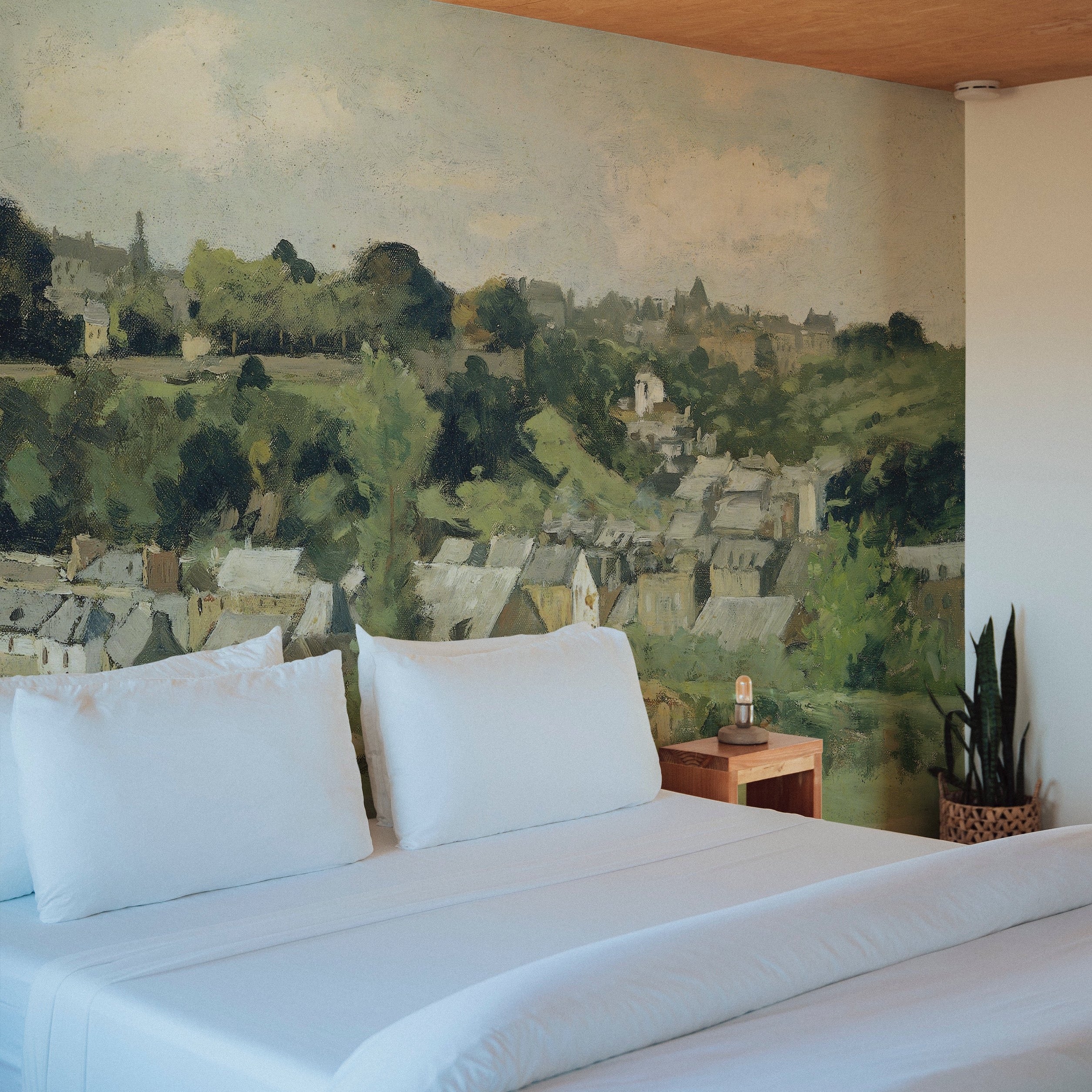 A bedroom setting enriched with a 'Views - Vintage Wall Mural', presenting a serene village scene. The mural serves as a stunning backdrop to a simple bed setup, complementing the room with its rich, earthy tones and peaceful landscape.