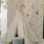 A child's play tent set against the Nursery Blooming Wallpaper, which features a soft, blooming floral pattern, providing a whimsical and enchanted setting for play and rest.