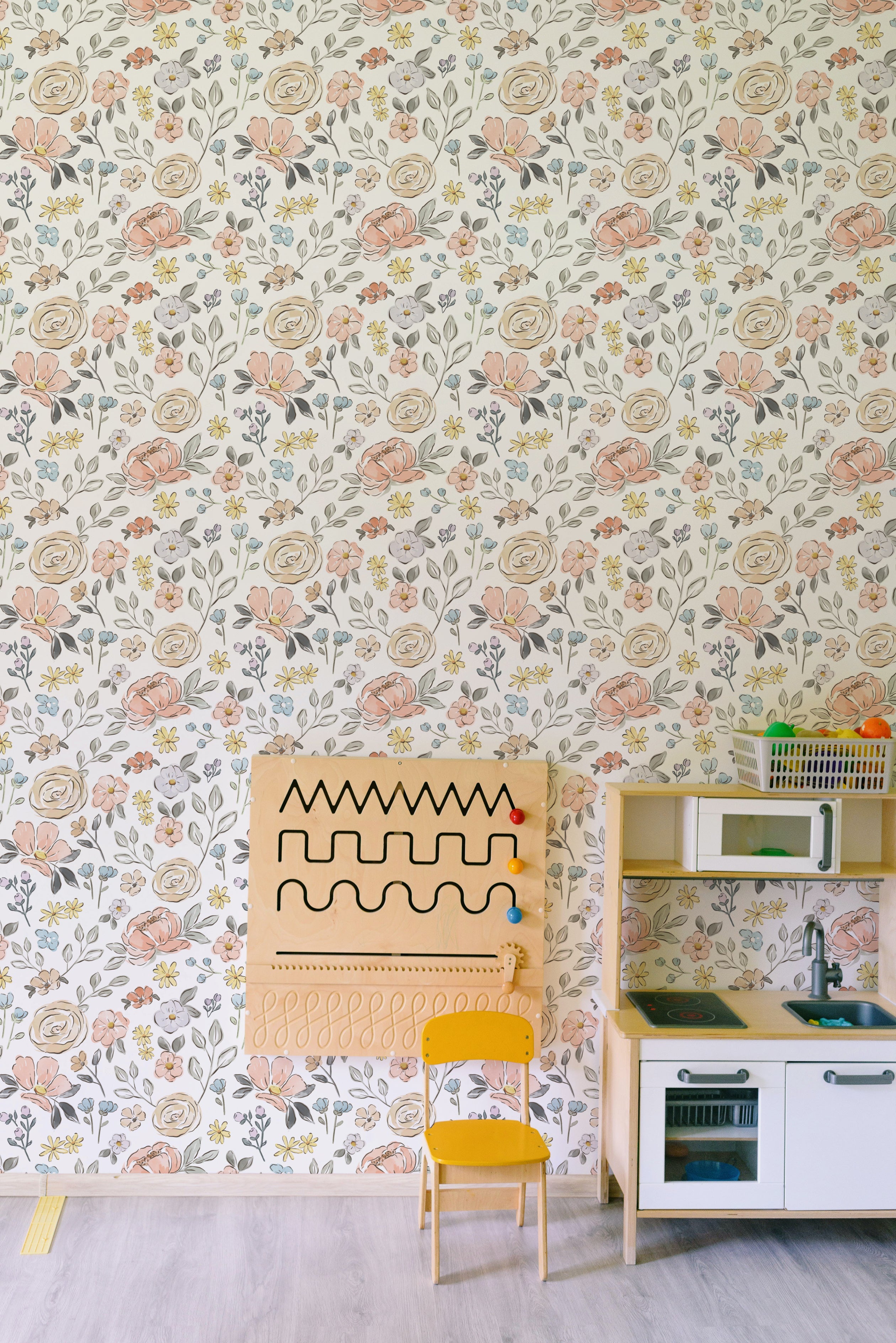 A serene workspace featuring the Nursery Blooming Wallpaper, adorned with a delicate floral pattern of pink and yellow flowers against a cream background, enhancing the creative charm of the space.