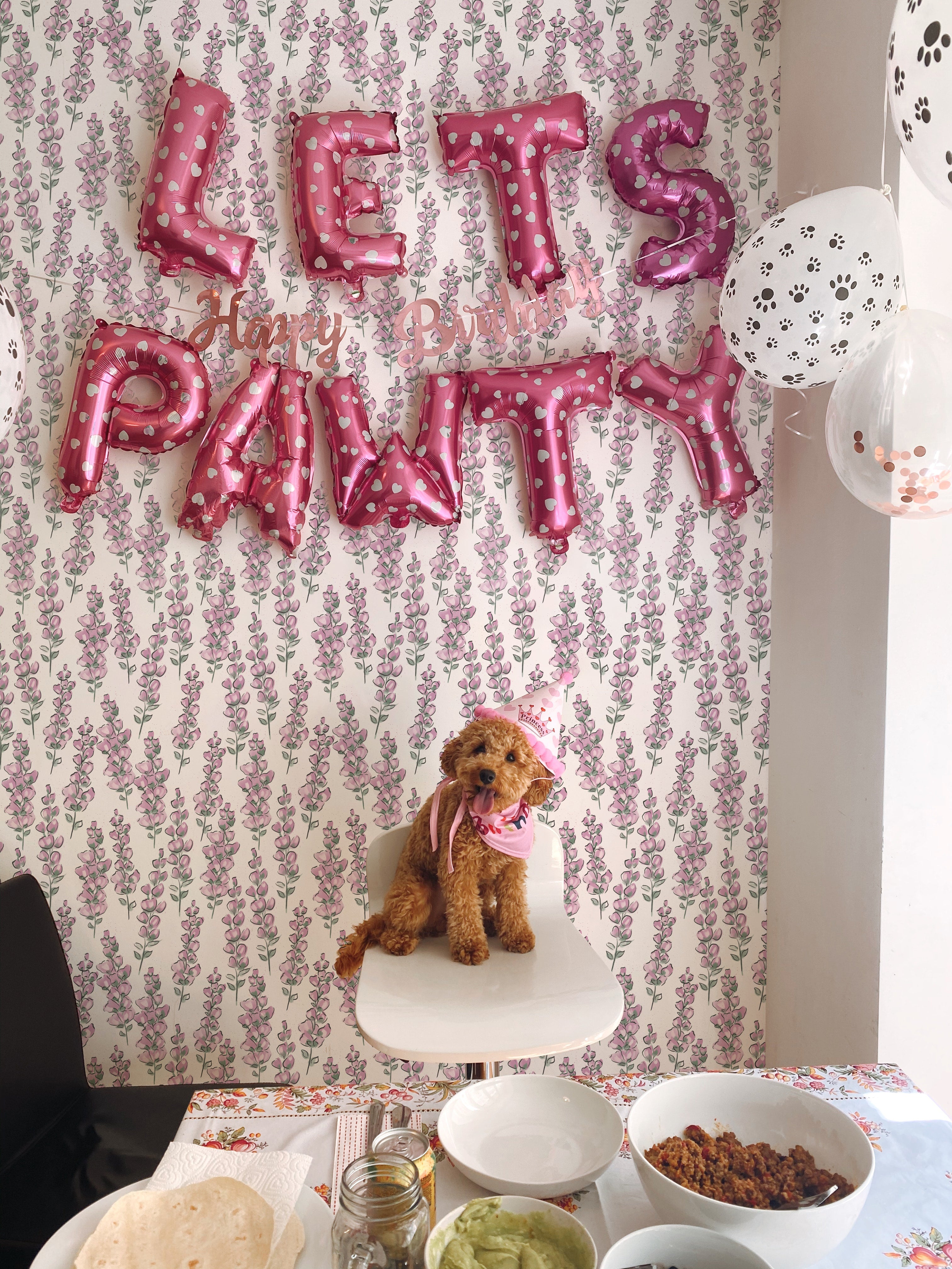 A playful nursery scene with the "Elegant Nursery Wallpaper" as a backdrop, featuring a dog with party hats under pink balloon letters spelling "LET'S PAWTY" for a birthday celebration, highlighting the versatility and charm of the wallpaper.