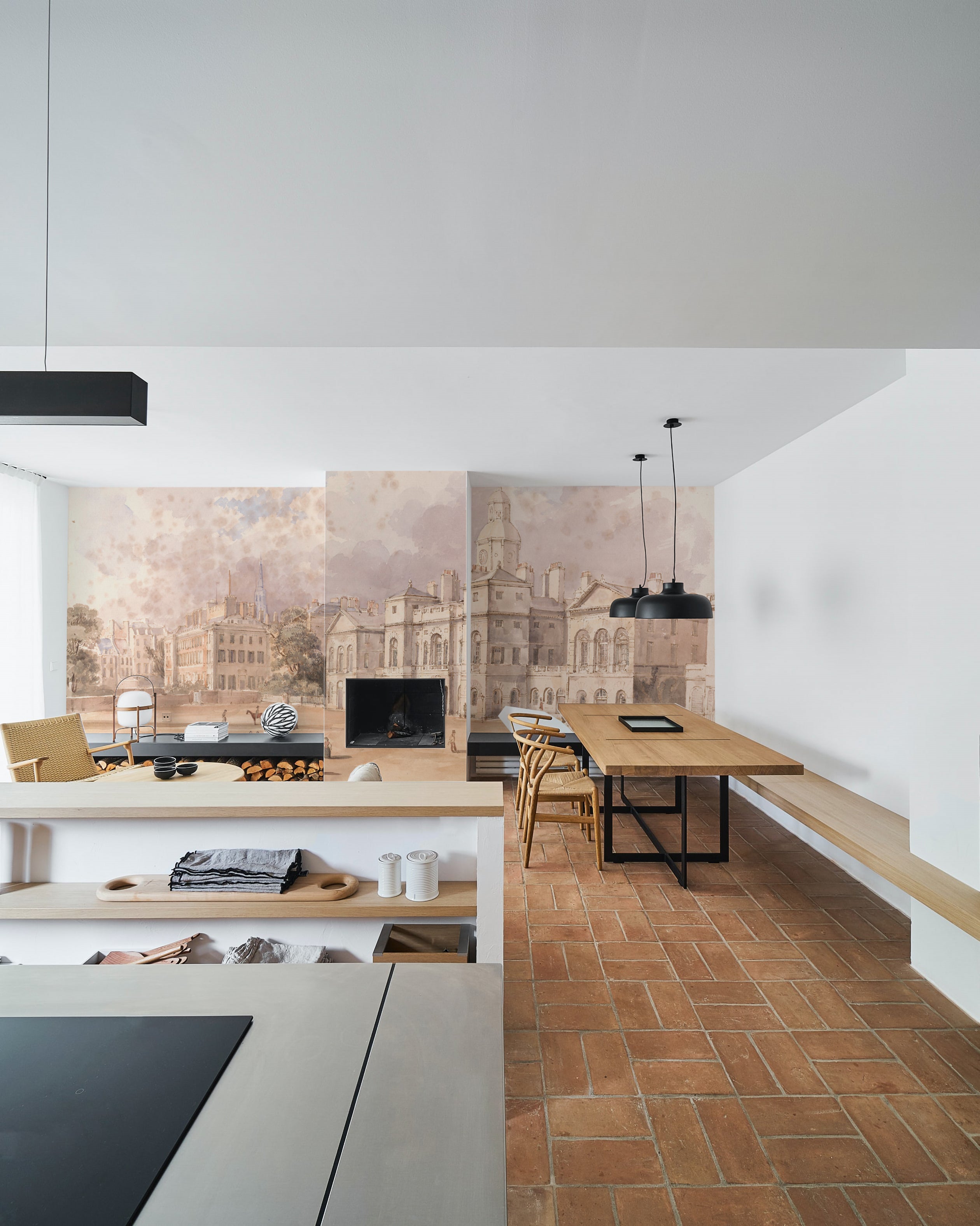 A modern kitchen and dining space fitted with terracotta tiles and contemporary furnishings, complemented by the "Parade" wallpaper mural portraying an antique city square, merging modern living with historical charm.