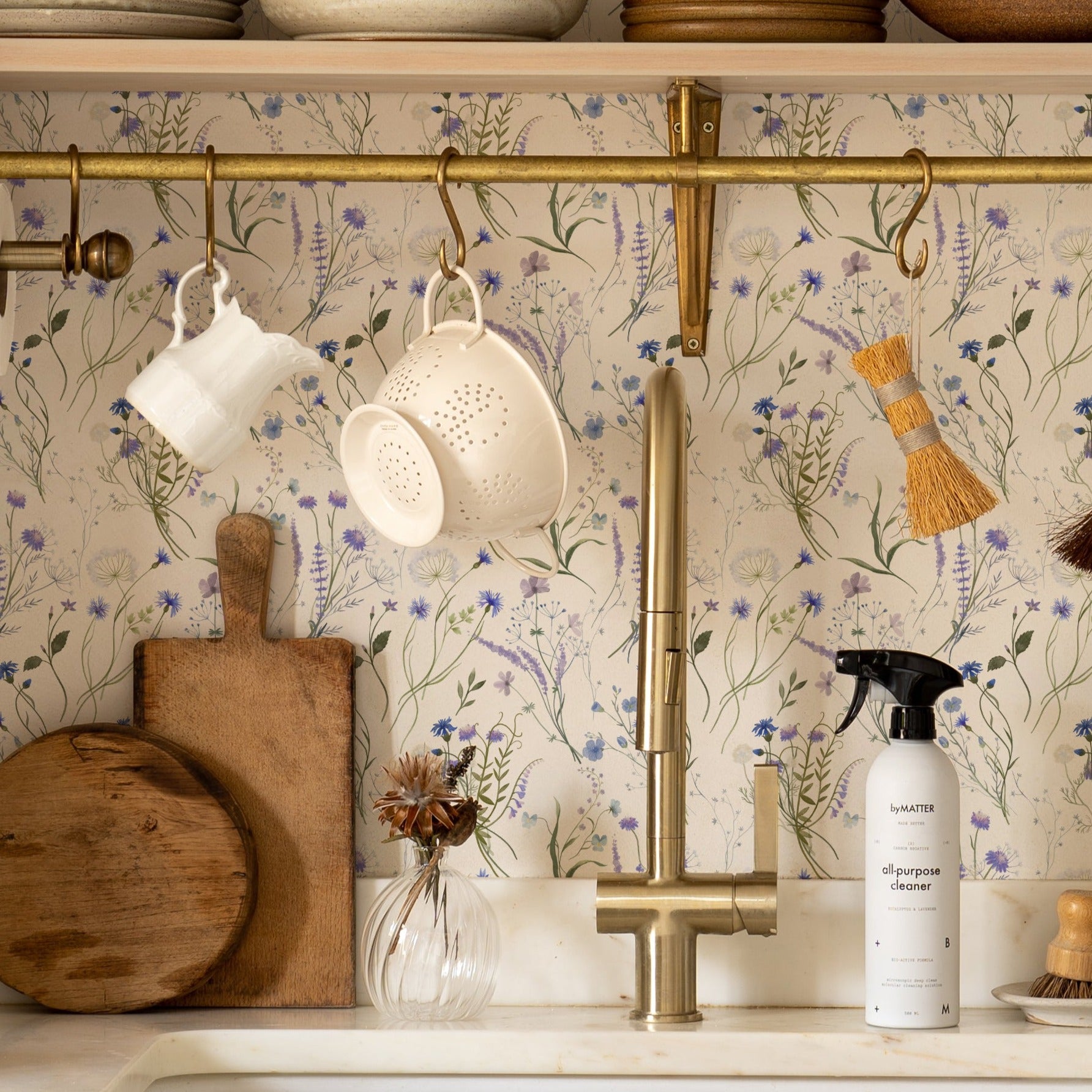 A charming kitchen setup enhanced by the Wildflower Bouquet Wallpaper. The wallpaper adds a burst of nature with its delicate floral design, paired beautifully with rustic kitchen accessories and utensils hanging against a floral backdrop.