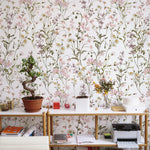 Workspace with WildFloral Wallpaper in the background, providing a vibrant and naturalistic feel to the room. The desk is cluttered with office supplies, a bonsai tree, and potted plants, which complement the floral motifs of the wallpaper