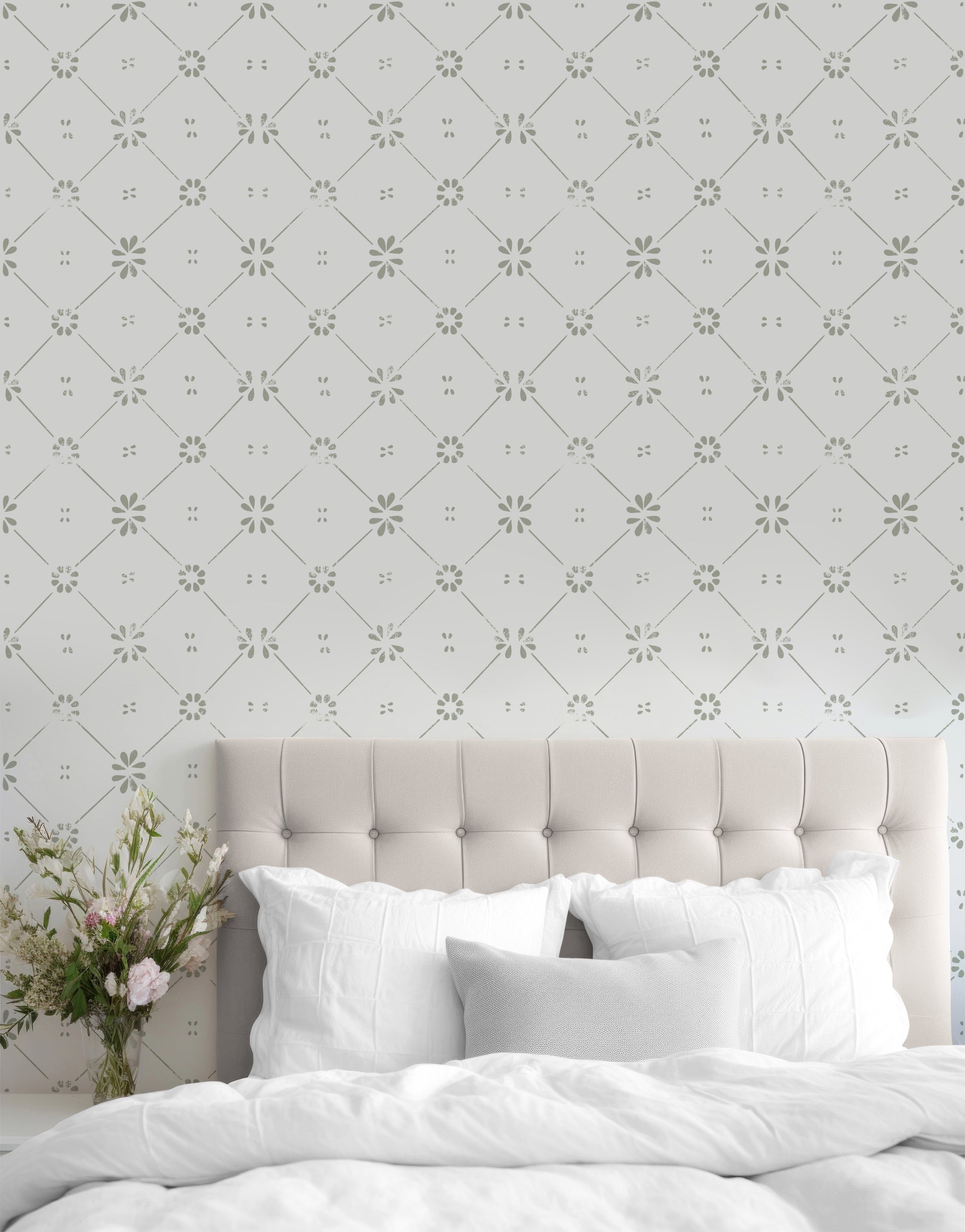A bedroom with the Floral Lattice Wallpaper adorning the wall behind a beige tufted headboard. The wallpaper features a repeating pattern of green flowers and lines on a white background, adding a touch of sophistication to the room. A vase with fresh flowers is placed on a bedside table.