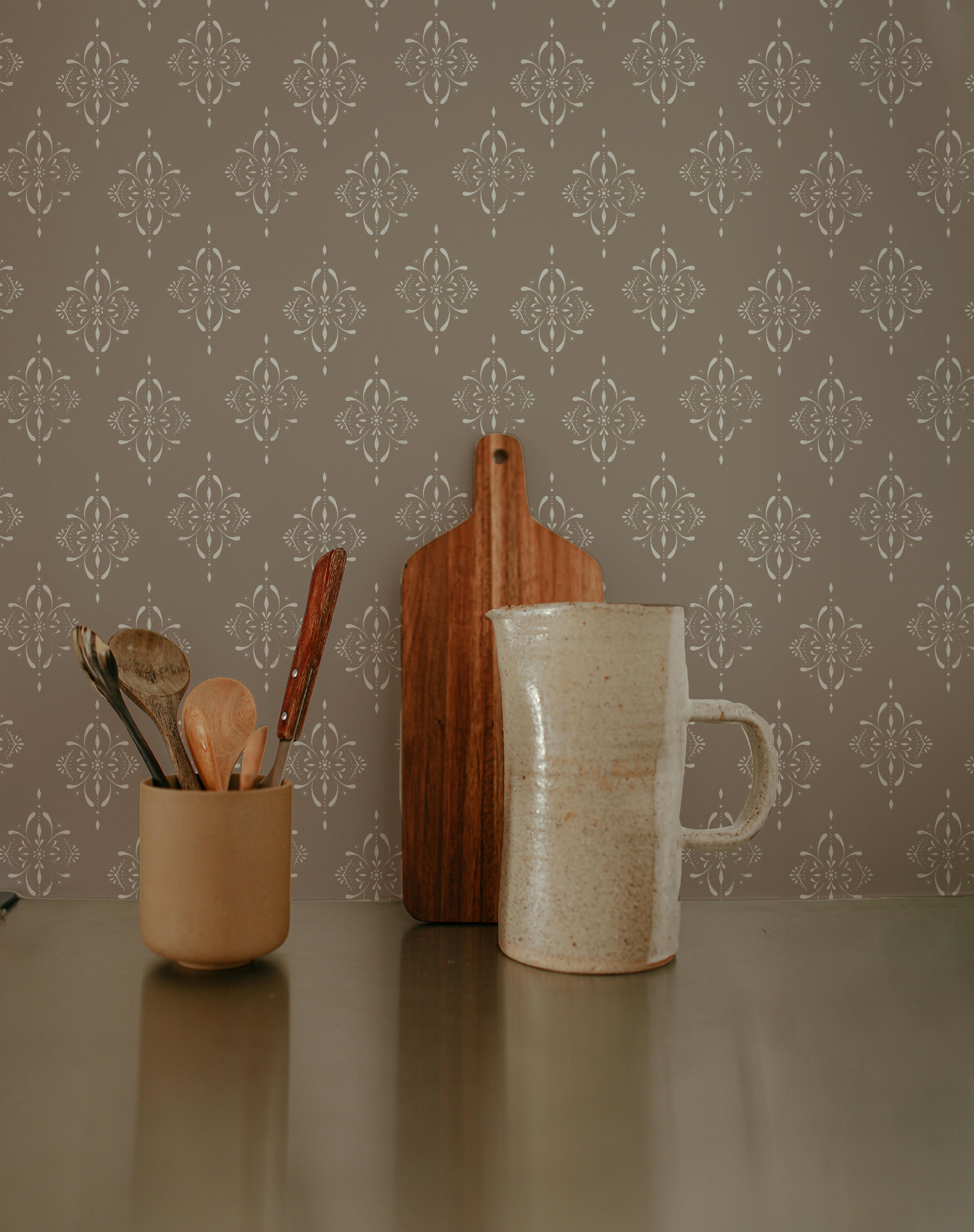 A stylish kitchen setup featuring rustic elegance wallpaper with a refined floral pattern and intricate medallions. The wallpaper, with its vintage charm, enhances the space's sophisticated look. On the countertop, there is a ceramic mug, a wooden cutting board, and a small cup holding wooden utensils, adding a touch of rustic elegance to the decor
