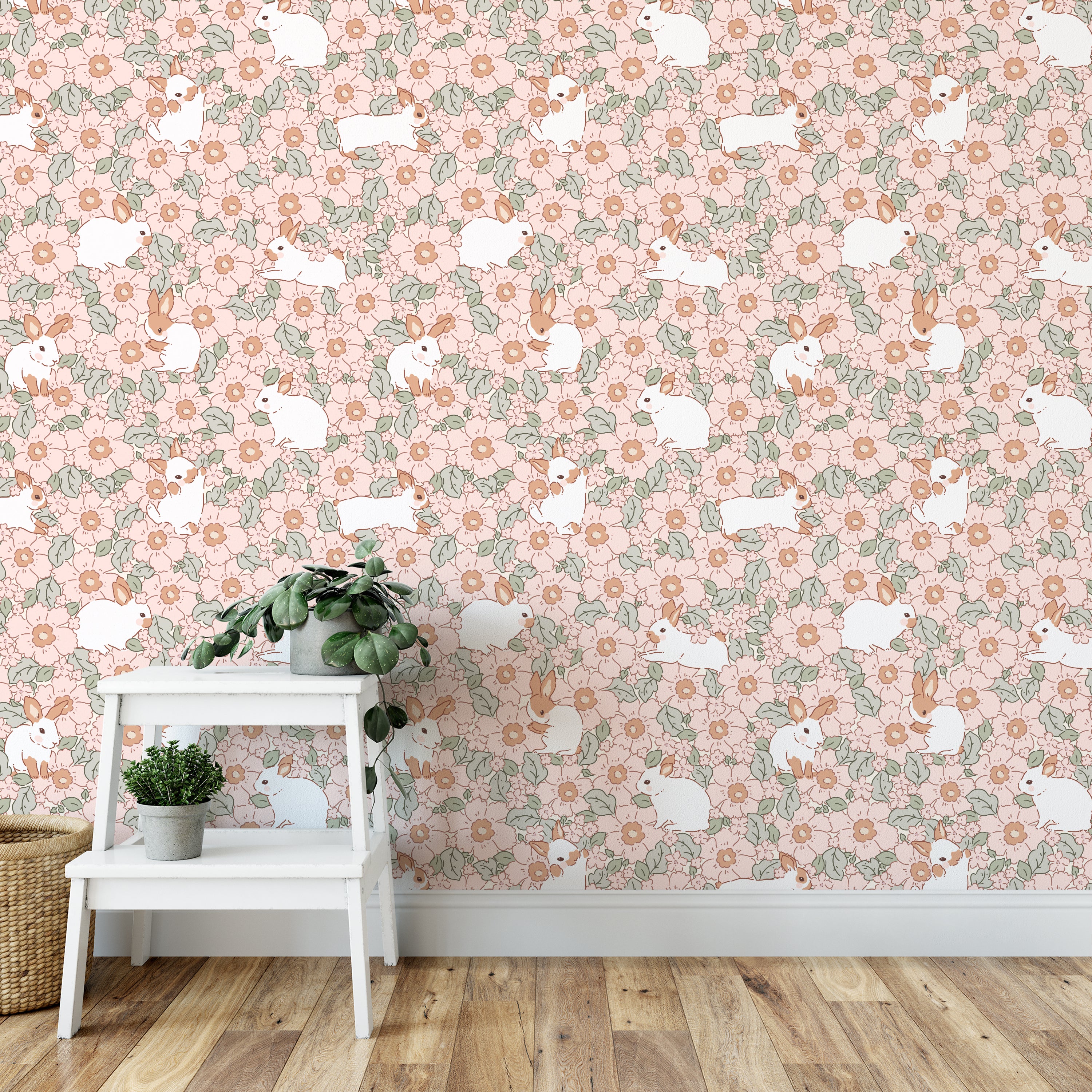This image captures a serene corner of a room decorated with the Petite Lapinou Wallpaper, featuring playful white rabbits interspersed among soft pink flowers and lush greenery. The setting includes a simple white plant stand with green plants, complementing the soft and inviting nature of the wallpaper.