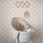 A nursery room beautifully decorated with Mini Floral Joy Wallpaper, displaying small pink and green floral motifs on a light beige background that complements the white wicker bassinet and cozy stuffed animals.