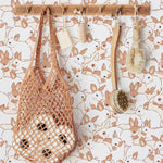 Interior decor scene showcasing the Lapinou Wallpaper with beige bunny patterns. A wooden rack holds various natural bath accessories including a mesh bag, a wooden brush, and two bars of soap, enhancing the rustic charm of the room.
