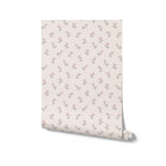 A roll of Chara Wallpaper laid out against a white background, showcasing a quaint pattern of pink floral sprigs with green leaves on a peach base. This wallpaper brings a fresh and soothing feel, ideal for creating a tranquil and beautiful space in your home.