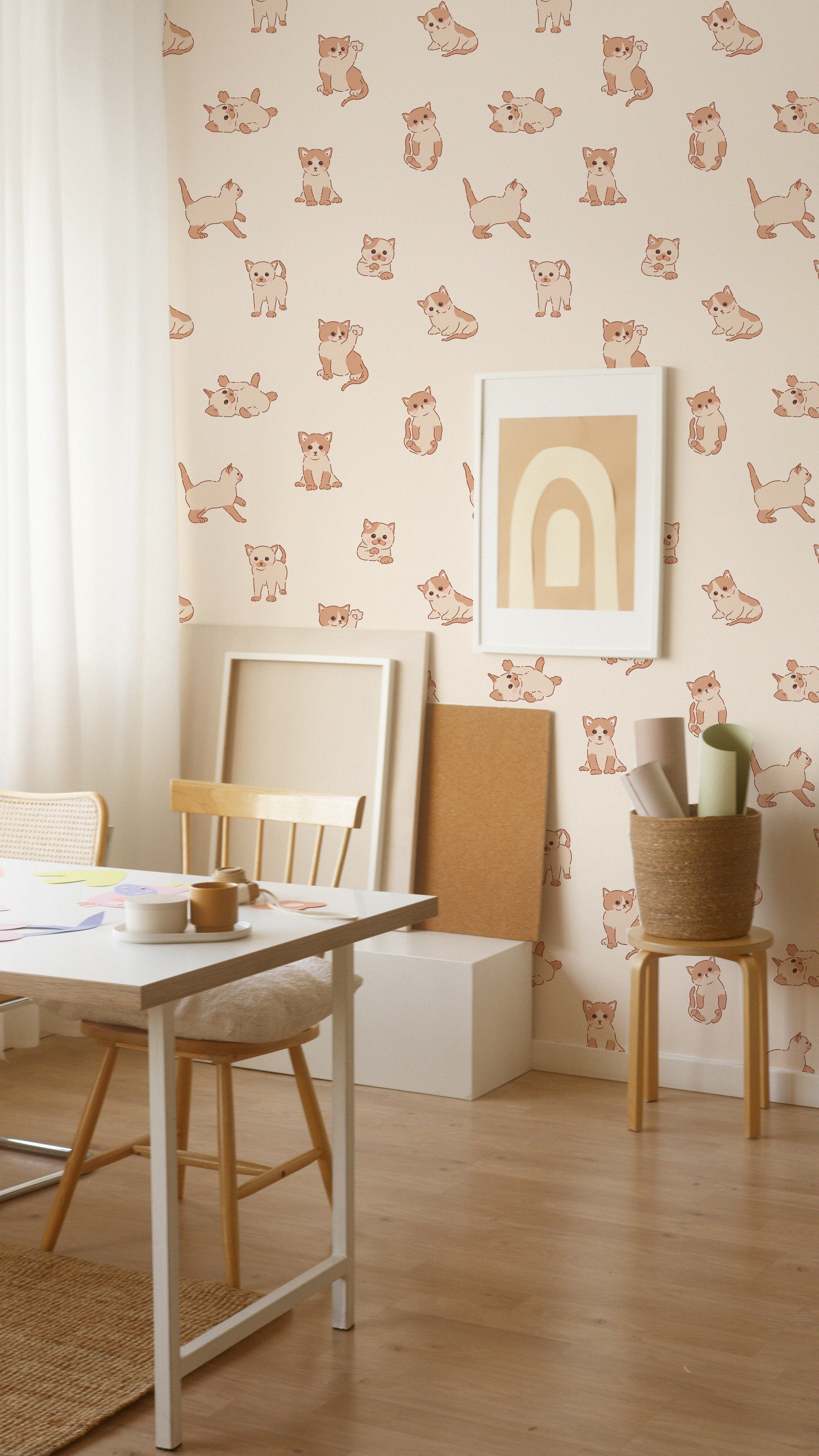 A creative workspace enhanced with Chaton Wallpaper displaying playful kitten illustrations in beige and brown on a peach backdrop. The room features a minimalist white desk, a light wooden chair, and various art supplies, creating an inspiring environment for creativity.