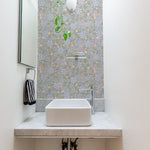 A small and elegant bathroom space enhanced with Joie Wallpaper, which features a beautiful floral pattern in shades of blue, pink, and green on a light green background. The room is fitted with a modern white sink on a marble countertop, under a skylight that adds natural light to the floral ambiance.