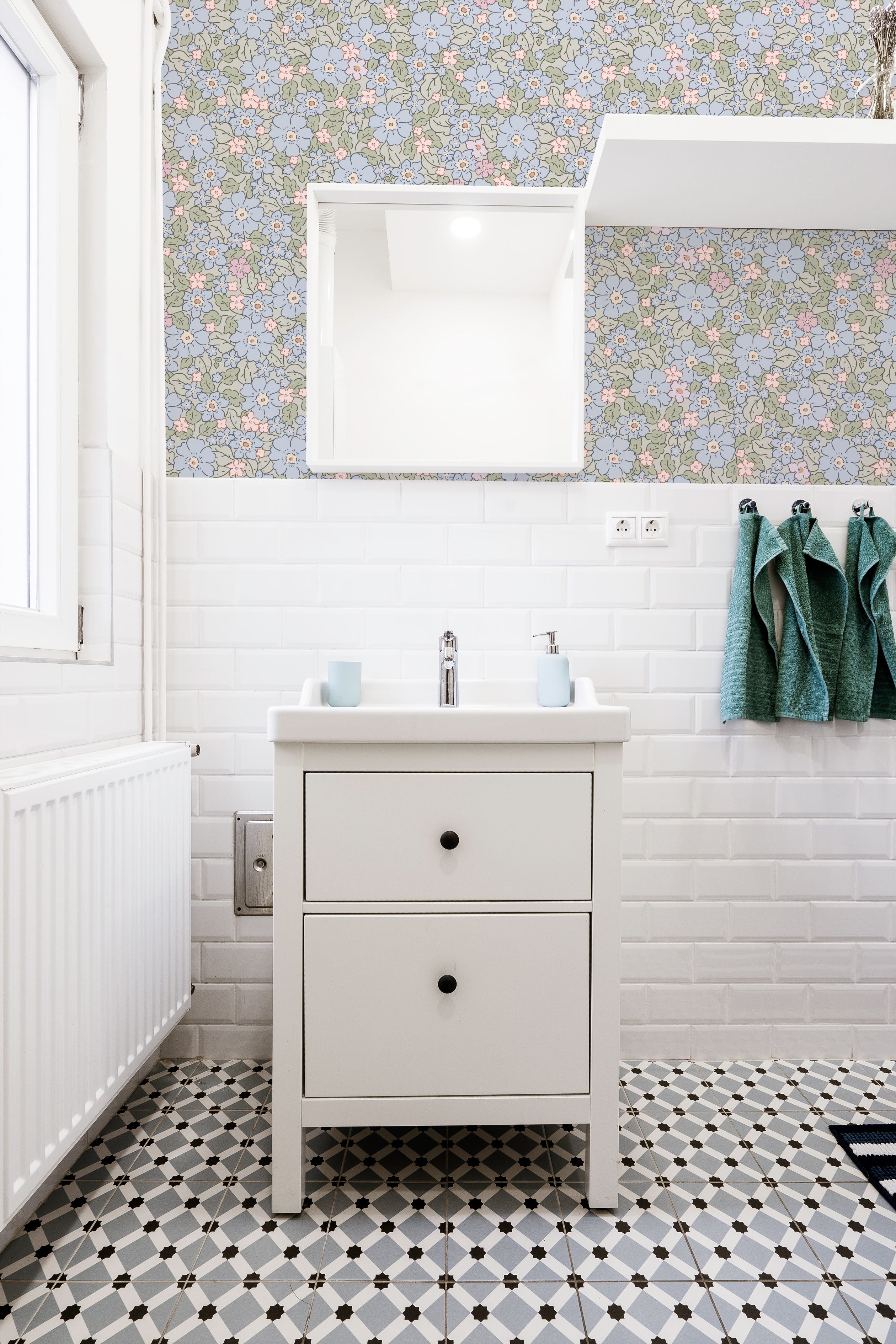 A vibrant bathroom decor showcasing Joie Wallpaper with a pattern of intricate multicolored flowers on a light green background. The setting includes a white sink cabinet with a top-mounted basin, complemented by white subway tiles and a black-and-white checkered floor, creating a bright and cheerful atmosphere.