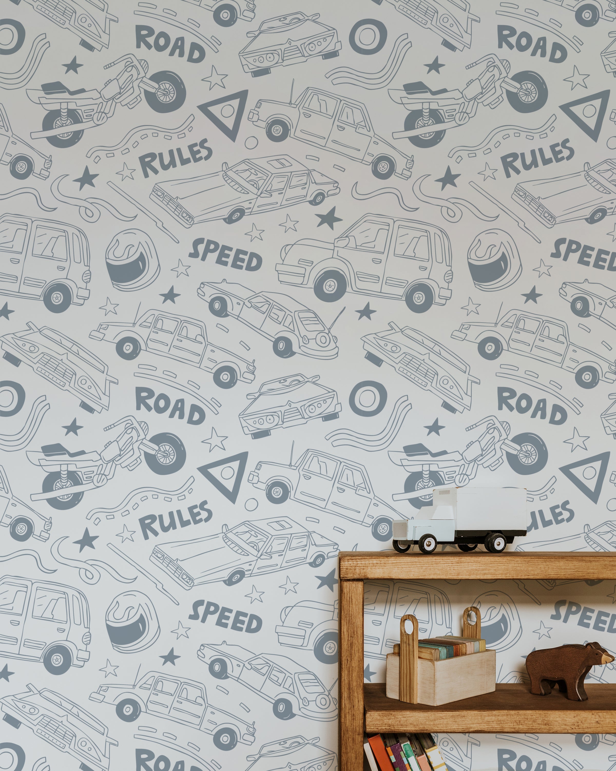 A children's room setup featuring a wooden shelf with toys and books. The background features Speedway Adventures Wallpaper with playful illustrations of various vehicles, roads, and road signs in light gray on a white background, creating a fun and energetic atmosphere for kids.