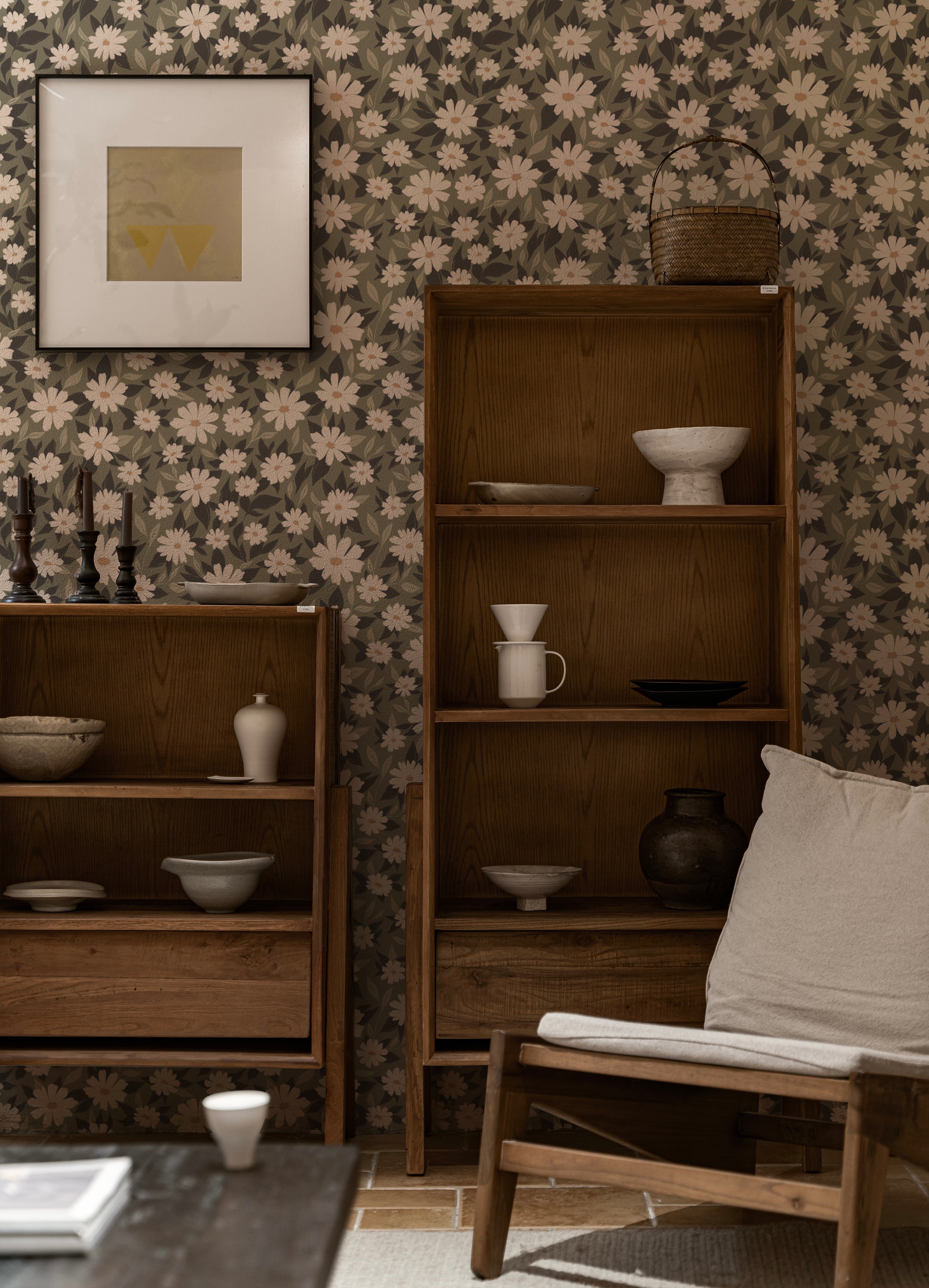 A sophisticated living space showcasing the "Daisy Blooms Wallpaper - 25"" on the walls, complemented by a wooden shelving unit displaying various pottery pieces. The naturalistic floral print enhances the room's rustic charm and creates a calming, elegant environment.