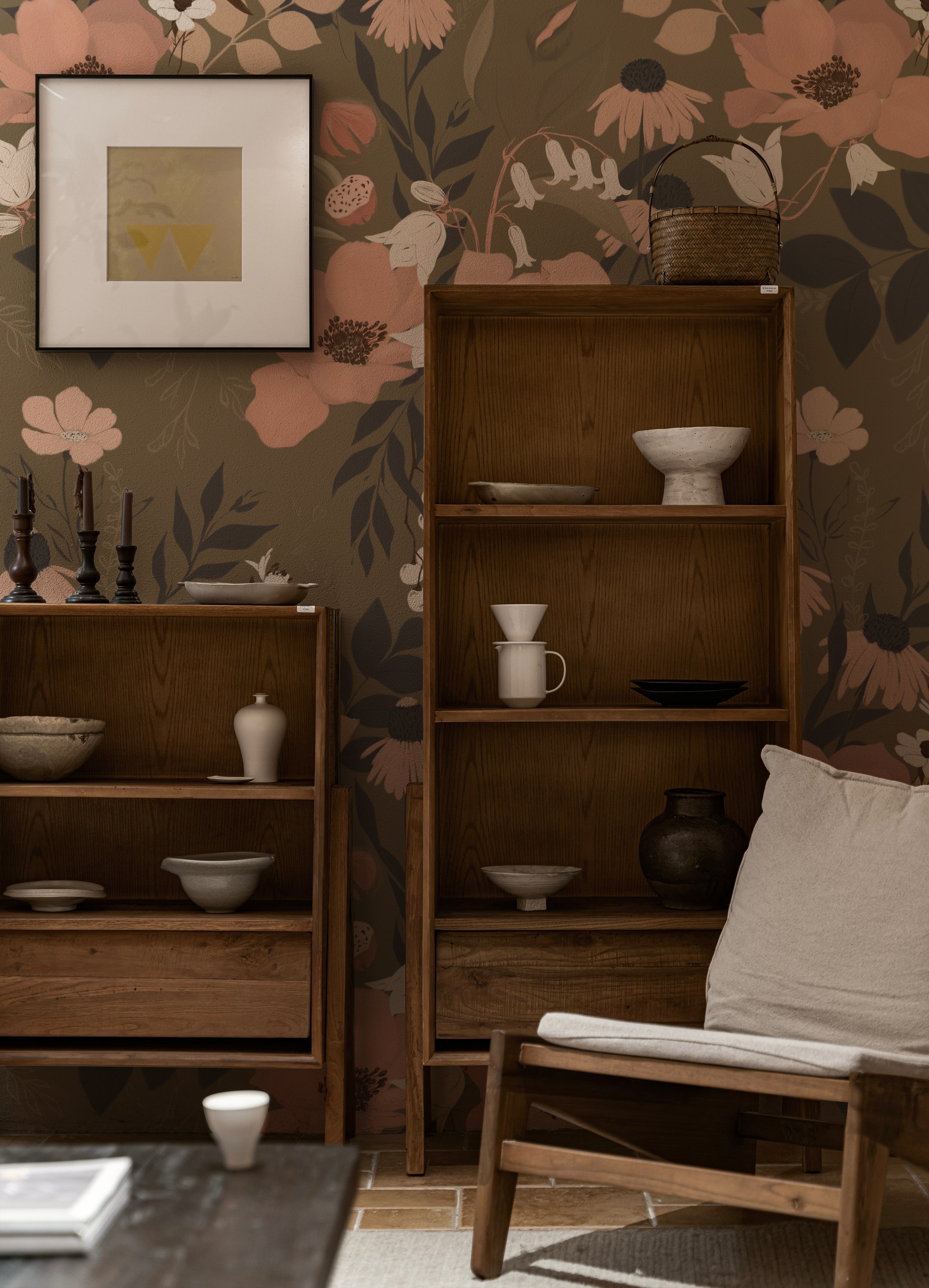 An interior scene featuring the Botanic Garden Wallpaper - 75" as a decorative backdrop in a cozy room setting. The wallpaper's large floral print in soft peach and muted green tones complements the wooden furniture and ceramic decor, enhancing the space's warm and inviting atmosphere.