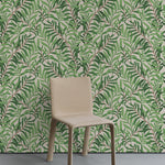 A minimalist room with a botanical wallpaper accent wall. The wallpaper showcases a dense pattern of green leaves on intertwining branches against a light beige background. The room features a simple beige chair placed in front of the wallpaper.