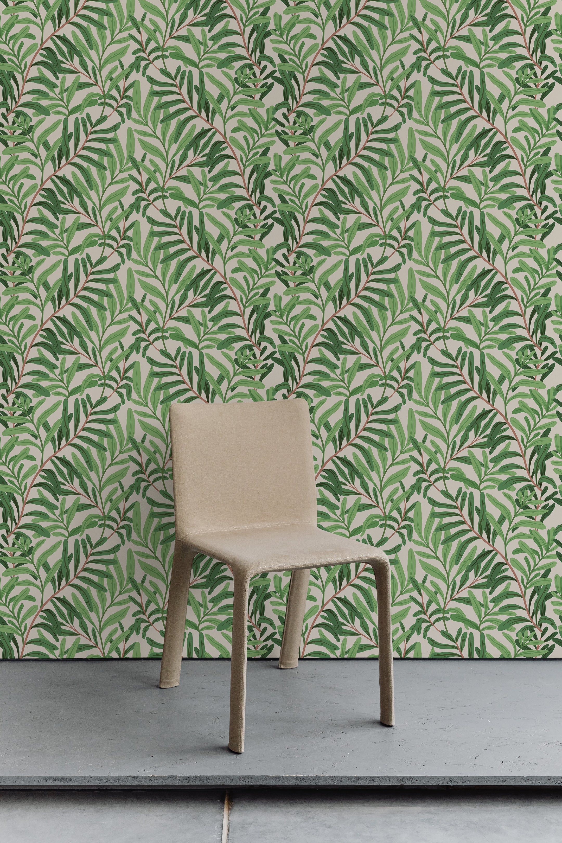 A minimalist room with a botanical wallpaper accent wall. The wallpaper showcases a dense pattern of green leaves on intertwining branches against a light beige background. The room features a simple beige chair placed in front of the wallpaper.