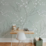 A modern workspace elegantly enhanced by the Enchanted Blossoms Wallpaper. The wallpaper forms a beautiful backdrop behind a minimalist wooden desk paired with a white modern chair. Simple office supplies and a vintage-inspired lamp complete the setup, emphasizing the wallpaper's ability to blend naturally into a stylish and functional area.