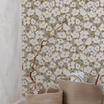 Interior scene with White Fleur Wallpaper featuring clusters of white flowers on slender branches, set against a muted olive background, complemented by two wicker baskets in the foreground.
