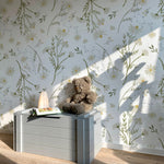 A child-friendly corner featuring the "Daisy Bouquet Wallpaper - Large" with sunlight filtering through a window casting shadows on the floral pattern. A cozy play area is set up with a grey toy box and a plush teddy bear, creating a peaceful and inviting space for play and relaxation.