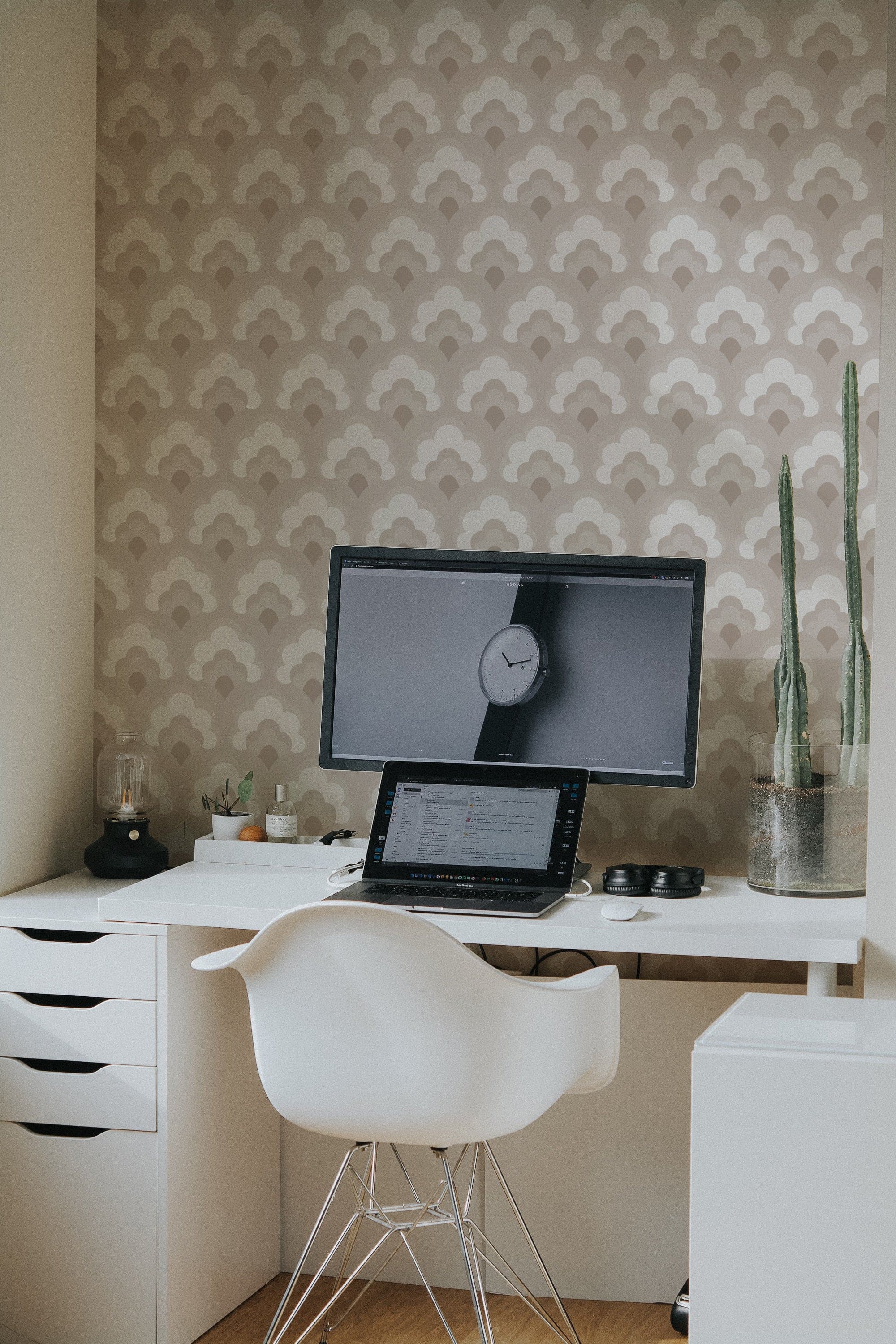 A modern home office setup with 'Scallop Mosaic Wallpaper' adorning the walls, featuring a repetitive beige and white scalloped design. The room is neatly organized with a white desk, a stylish ergonomic chair, and a desktop setup, offering a calm and chic workspace.